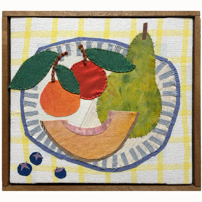 Fruit Bowl textile collage by artist Hannah Goff. The artwork is comprised of hand-sewn and painted, reclaimed and recycled fabrics. It features a pear, cantaloupe slice, a peach, and an apple in a bowl, with three blueberries to the side. Finished in a handmade rustic wood frame.