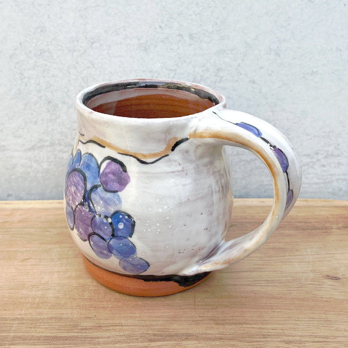 Handmade ceramic mug by NC potter Molly Lithgo. White with grapes decoration. View two with handle detail.