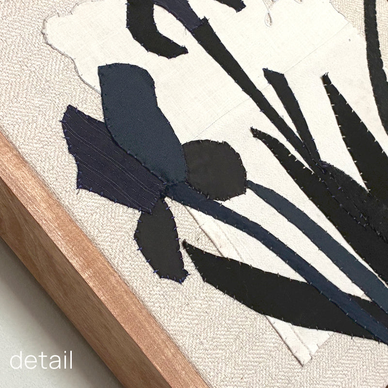 Framed textile artwork of black iris flowers on a textured beige background by Hannah Goff. Close up detail with frame. 