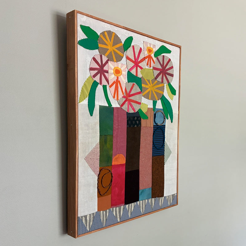 Artwork by Hannah Goff. Mixed media textile painting with geometric vase and colorful abstracted flowers. Side view on wall. 