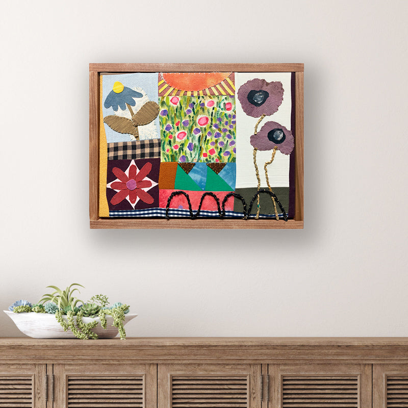 Poppy Patchwork, multicolored floral mixed media textile artwork by Hannah Goff with handmade wood frame. Displayed over table. 