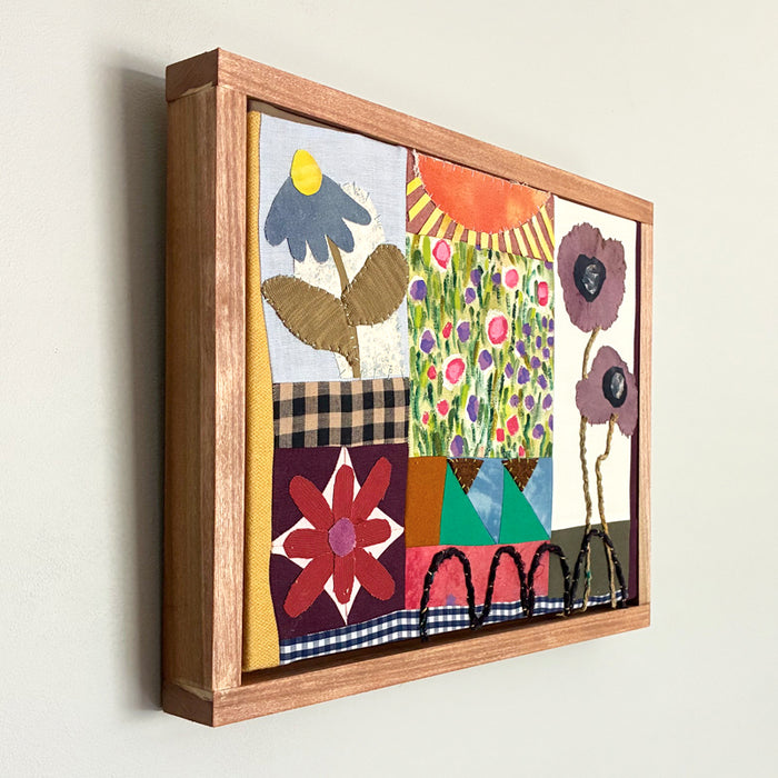 Poppy Patchwork, multicolored floral mixed media textile artwork by Hannah Goff with handmade wood frame. Side view on wall.