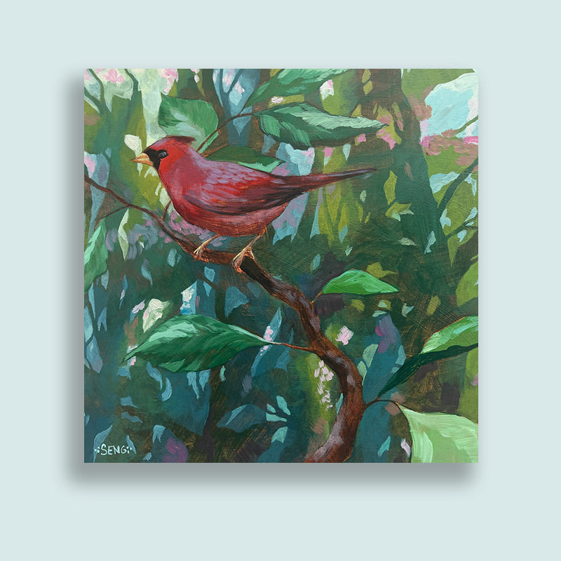 Acrylic painting of a cardinal perched on a branch, surrounded by green foliage. Artwork by Hannah Seng, displayed on pale blue wall. 