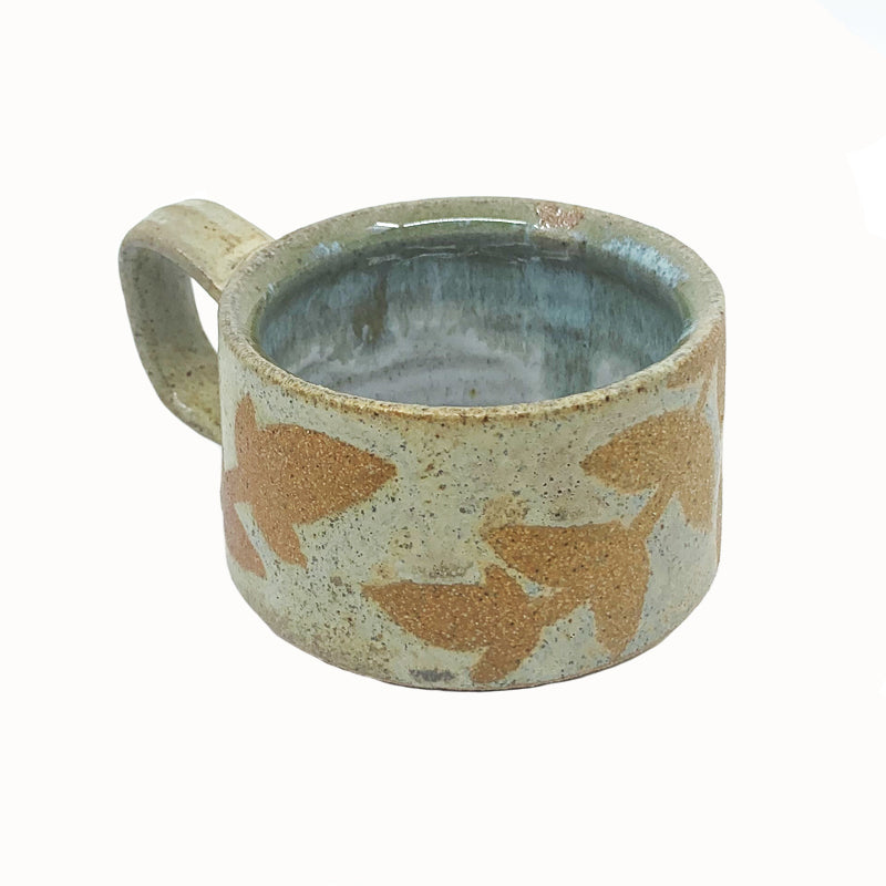 Heather Ossandon handmade, woodfired mug, angled view. Cream with light rust botanical pattern.