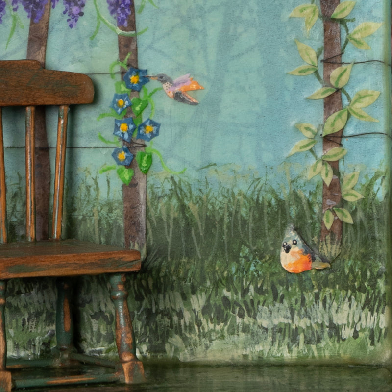 "A Gathering of Feathered Friends", mixed media assemblage inside a vintage wood box with finial on top. The artwork features a blue sky, a variety of birds, flowers on a fence post and a vintage dollhouse chair. By artist Janet Eskridge, close up detail shown.