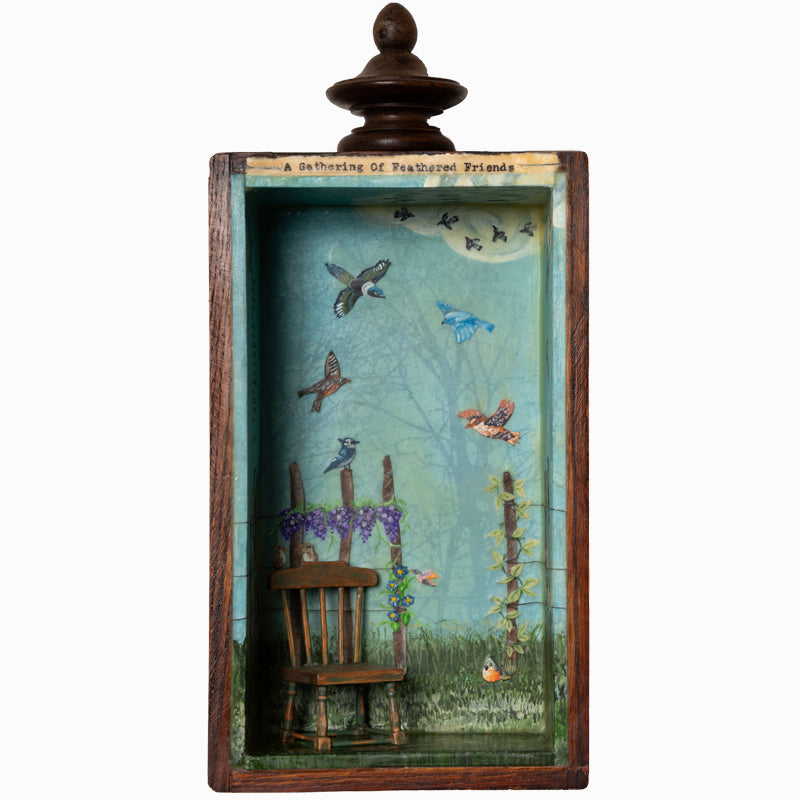 "A Gathering of Feathered Friends", mixed media assemblage inside a vintage wood box with finial on top. The artwork features a blue sky, a variety of birds, flowers on a fence post and a vintage dollhouse chair. By artist Janet Eskridge.