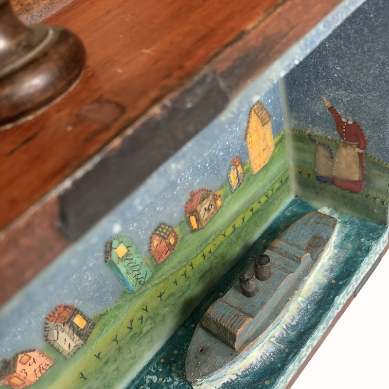 Interior detail of "By the Stars" mixed media encaustic assemblage by Janet Eskridge. A row of houses under a star filled sky, with a wooden boat in the water. 