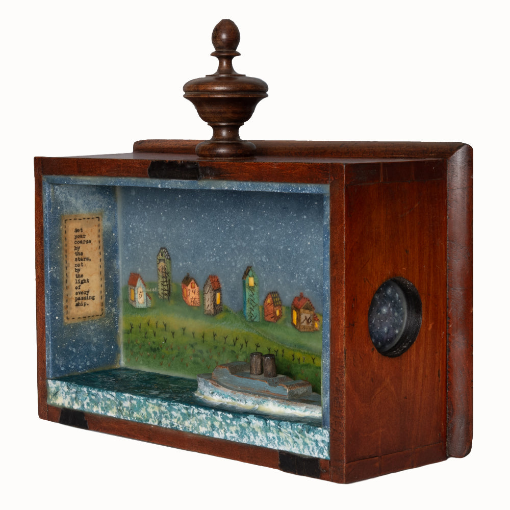 "By the Stars" mixed media encaustic assemblage by Janet Eskridge, side view. A wooden box with top finial, Janet's artwork fills the interior - a row of houses under a star filled sky, with a wooden boat in the water. 