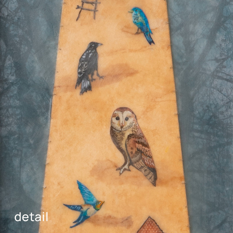 "Homecoming" mixed media assemblage by Janet Eskridge. A figure  in dress holds a bird's next. The dress is decorated with a rainbow, and various birds. The artwork is set inside a vintage wood box with a finial on top. Detail of various birds on the dress.