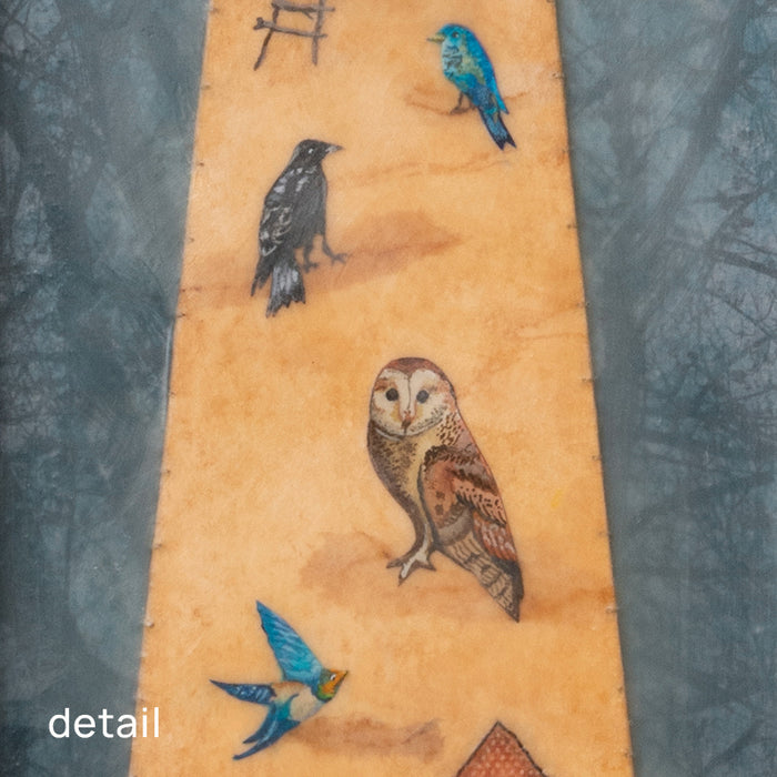 "Homecoming" mixed media assemblage by Janet Eskridge. A figure  in dress holds a bird's next. The dress is decorated with a rainbow, and various birds. The artwork is set inside a vintage wood box with a finial on top. Detail of various birds on the dress.