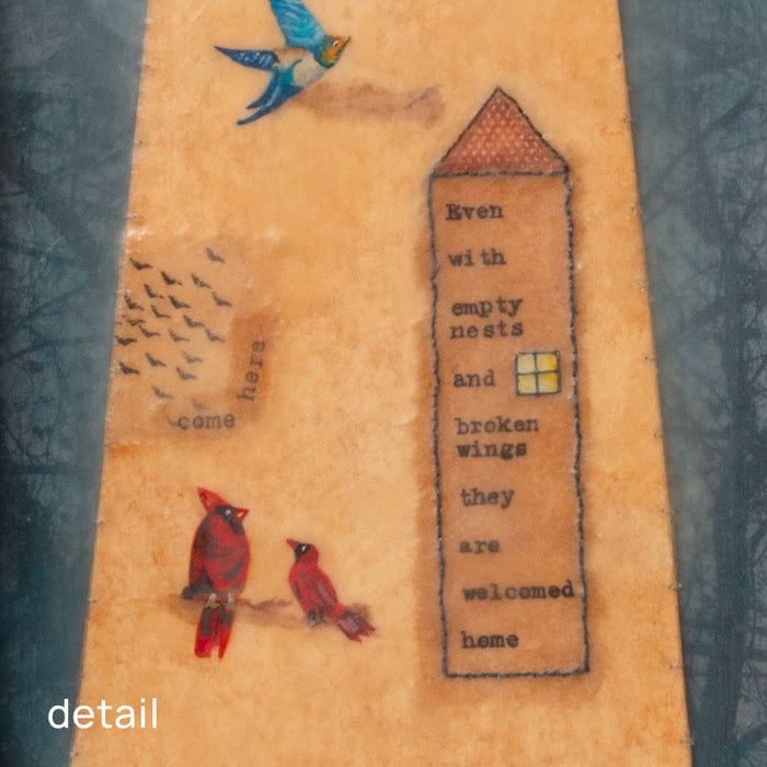 "Homecoming" mixed media assemblage by Janet Eskridge. A figure  in dress holds a bird's next. The dress is decorated with a rainbow, and various birds. The artwork is set inside a vintage wood box with a finial on top. Detail shown.