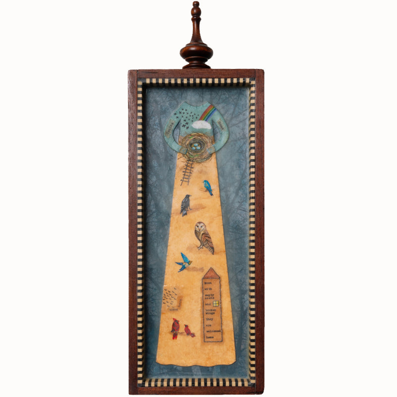 "Homecoming" mixed media assemblage by Janet Eskridge. A figure  in dress holds a bird's next. The dress is decorated with a rainbow, and various birds. The artwork is set inside a vintage wood box with a finial on top. 