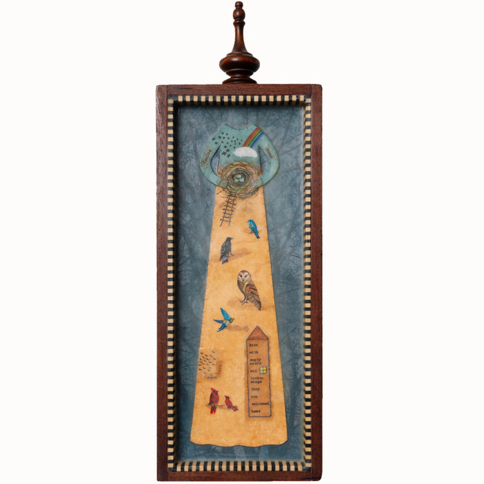"Homecoming" mixed media assemblage by Janet Eskridge. A figure  in dress holds a bird's next. The dress is decorated with a rainbow, and various birds. The artwork is set inside a vintage wood box with a finial on top. 