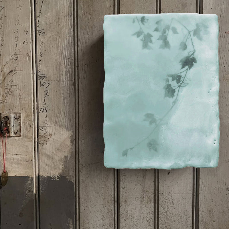 Mixed media encaustic painting by Liberty Hanson Wild in pale green and white with leafy branch detail. Shown on rustic wall. 