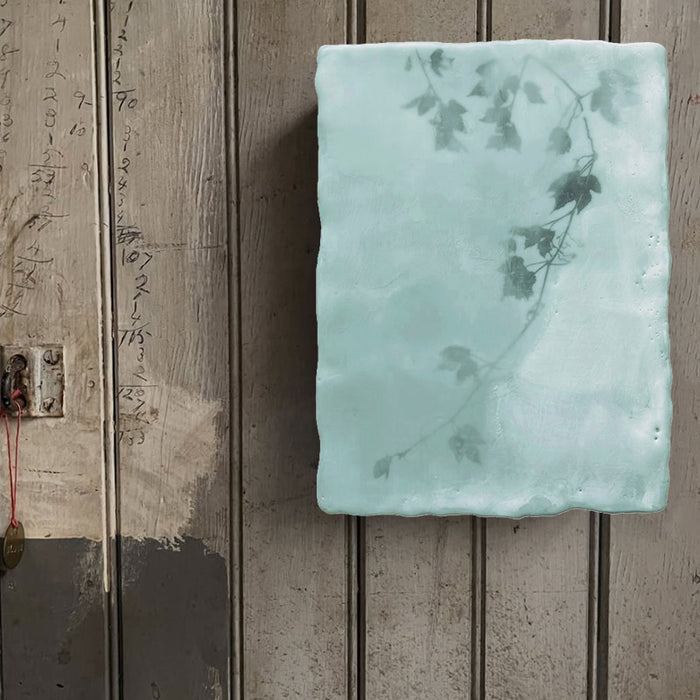 Mixed media encaustic painting by Liberty Hanson Wild in pale green and white with leafy branch detail. Shown on rustic wall. 