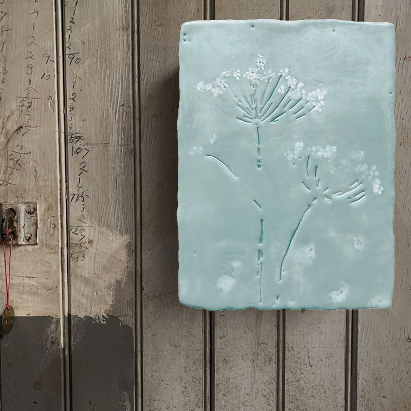 Mixed media encaustic painting by Liberty Hanson Wild in soft blue greens and white with embossed botanical detail. Artwork displayed on rustic wood wall. 