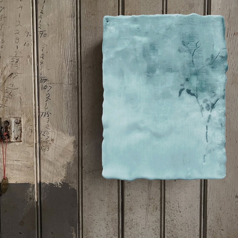 Mixed media encaustic painting by Liberty Hanson Wild in soft blue greens with leafy branch detail. Displayed on rustic wood wall.