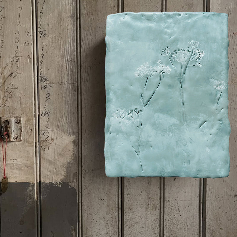 Mixed media encaustic painting by Liberty Hanson Wild in soft blues with  embossed botanical detail. Displayed on rustic wall. 