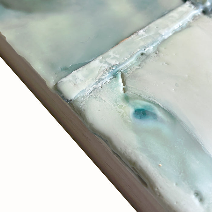 Mixed media encaustic artwork with creamy white and pale green leaf pattern. Close up view. 