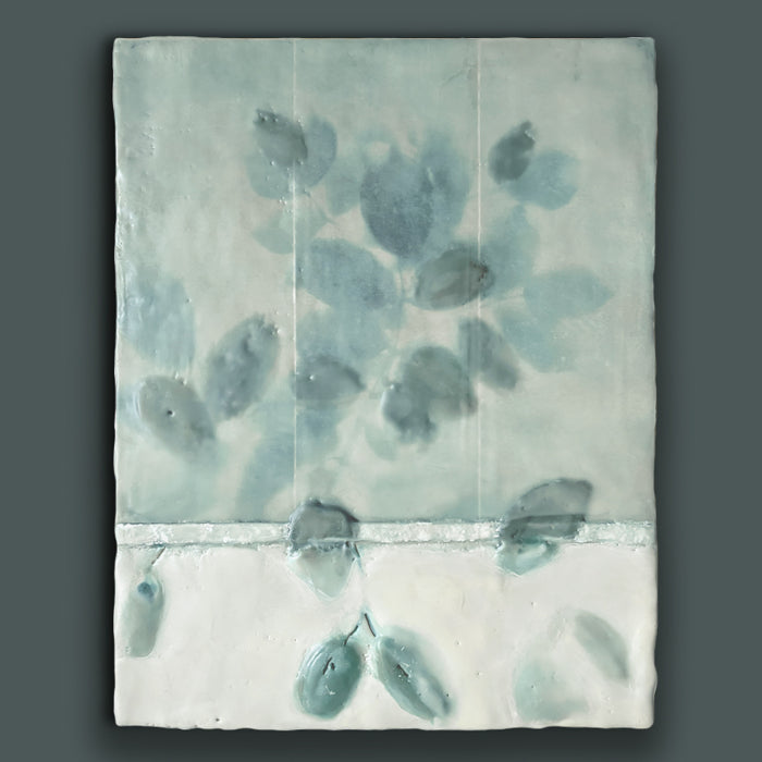 Mixed media encaustic artwork with creamy white and pale green leaf pattern. Painting shown on dark teal wall. 