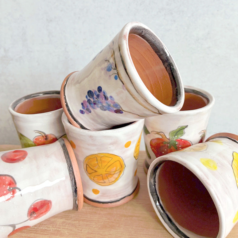 Small handmade ceramic cups by Molly Lithgo, white glazed with various fruit decoration. 