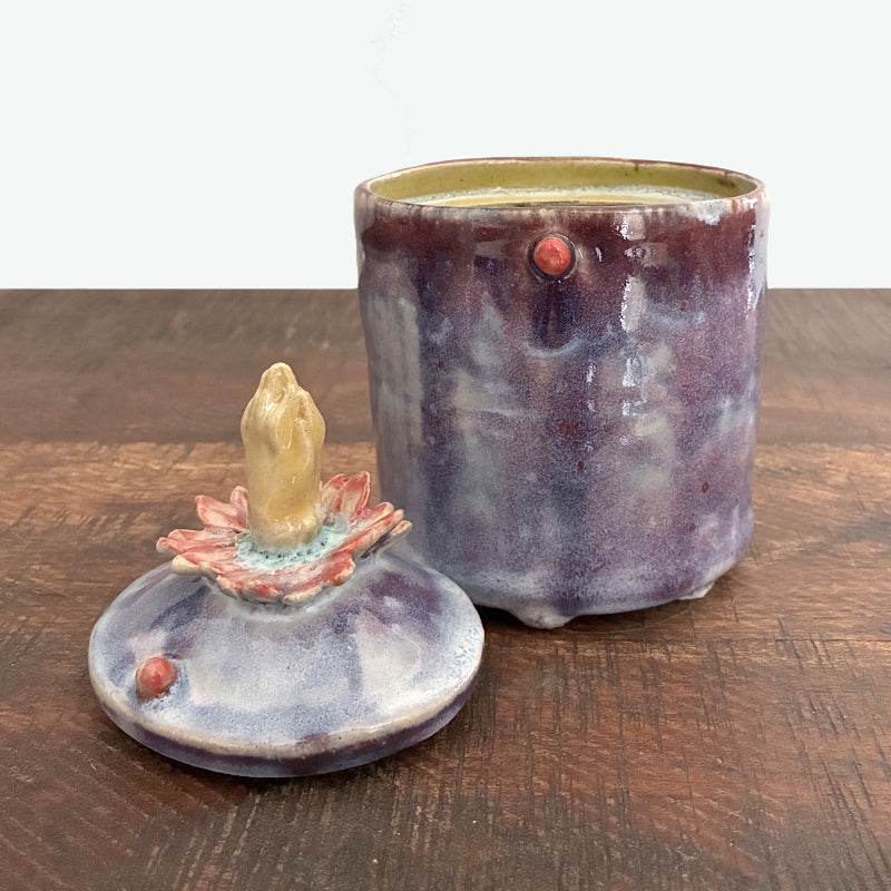 Small purple handmade ceramic jar with lid, lid has flower and hand detail. Image with lid off. 
