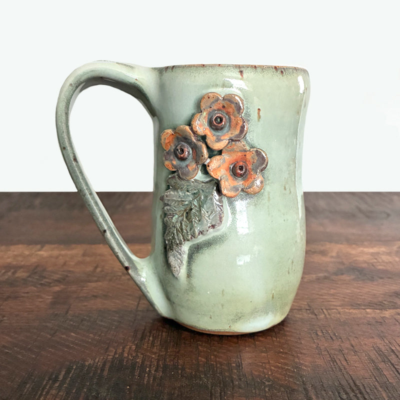 Handmade ceramic mug by Paula Smith. Pale, earthy green with pink flower and leaf details on both sides.
