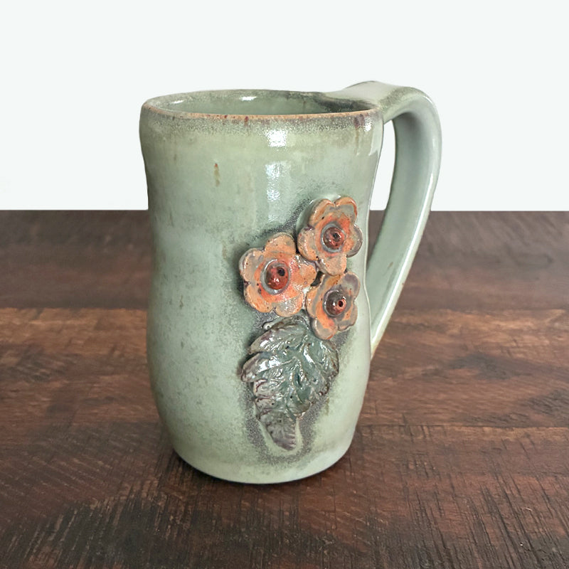 Handmade ceramic mug by Paula Smith. Pale green with pink flower and leaf details on both sides.