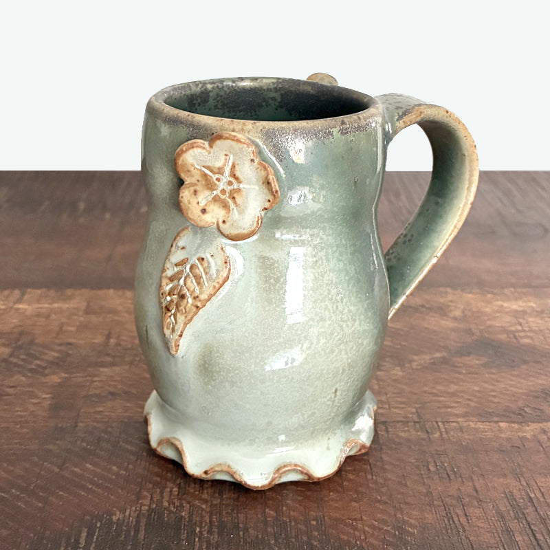 Handmade ceramic mug with flower and leaf detail and wavy bottom made by Paula Smith. 
