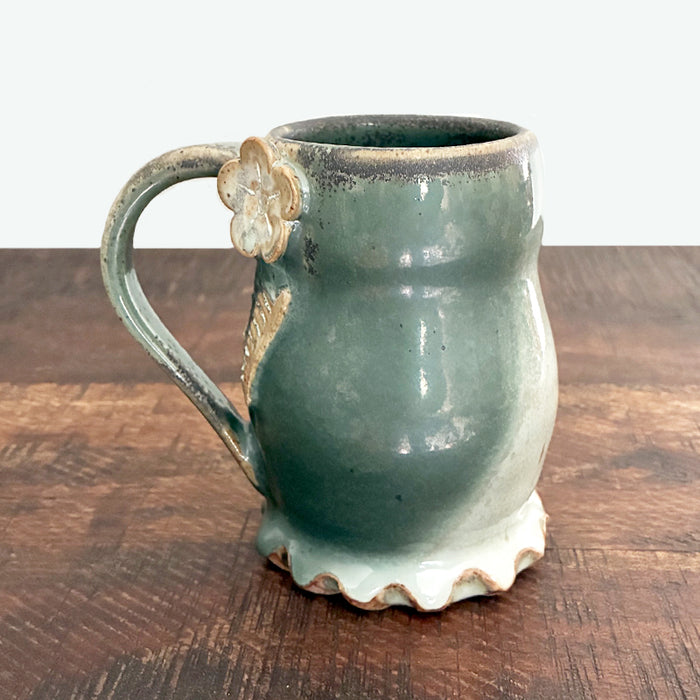 Handmade ceramic mug with flower and leaf detail and wavy bottom. 