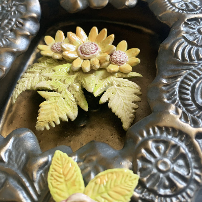 Handmade ceramic wall niche with flower details by Paula Smith. Gunmetal glazed clay with stamped details, with three dimensional yellow flowers and leaves. Interior flower detail.