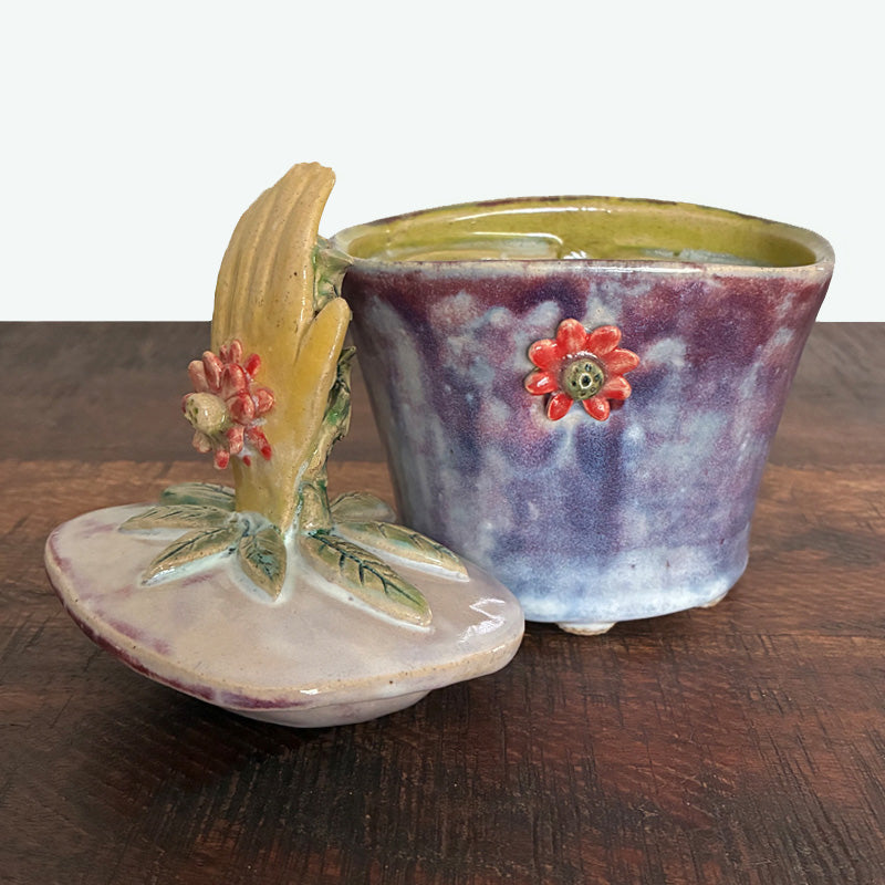 Purple handmade ceramic lidded jar with hand, rooster and flower details. Shown with lid off. 