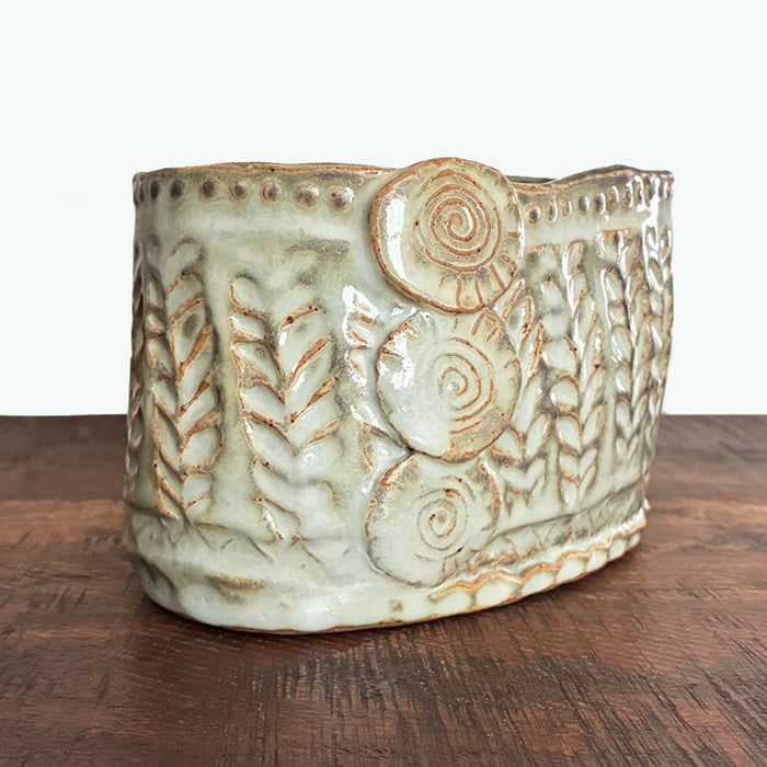 Handmade ceramic oval container with texture details. Side view. 