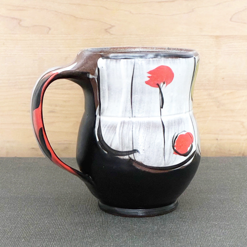 Handmade ceramic mug, black and white with abstracted orange floral design with green leaves by Renata Copeland. 