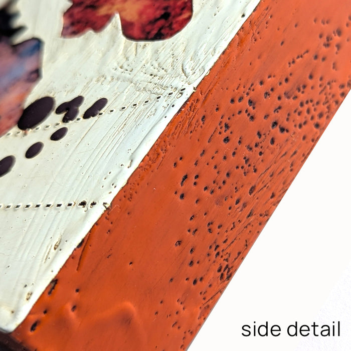 Bloom No. 13, small mixed media painting by artist Sarah Treanor. Red and purple textural, floral artwork created with digital prints of the  artist's cyanotypes and eco prints underneath layers of encaustic paint, with splatters of purple encaustic on top. Side detail shown.