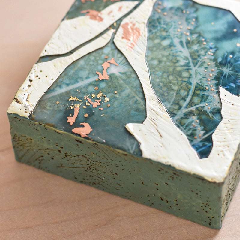 Midnight Embers V mixed media encaustic leaf artwork in rich blues with gold and copper leaf details. Close up view. 