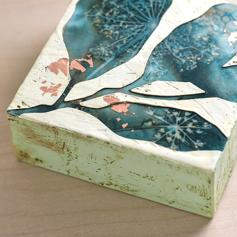 Midnight Embers VI mixed media encaustic leaf artwork in rich blues with gold and copper leaf details. Close up view.