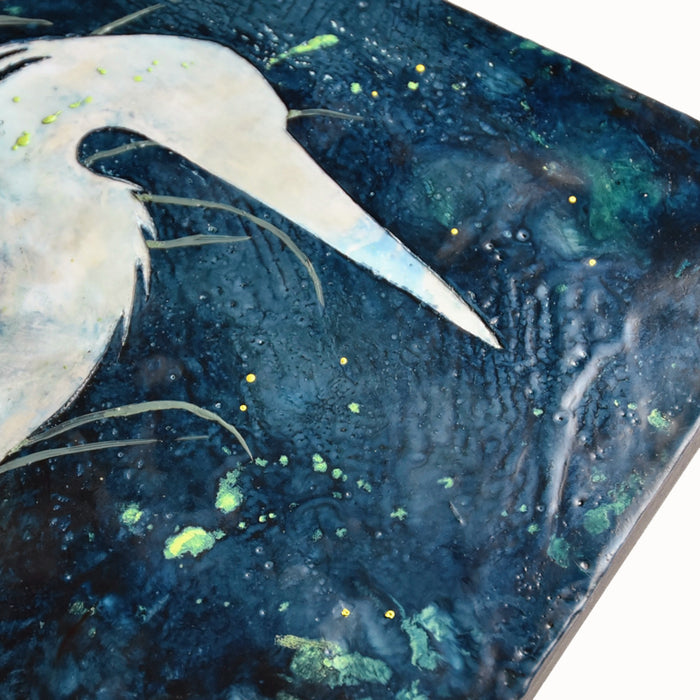 A white heron sitting among green leaves under a dark blue sky. Encaustic and eco print artwork by Sarah Treanor at Lark & Key, Charlotte NC. Detail to show texture.