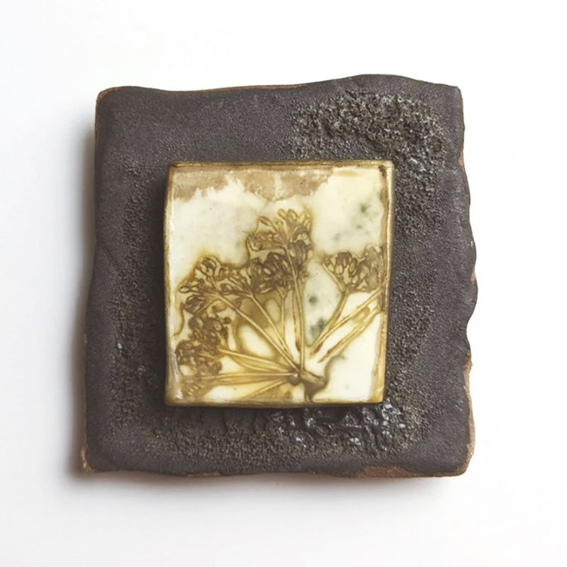 Small ceramic tile with textured blue glaze, with a botanical print encased in wax set in the center. Artwork by Sarah Treanor. 