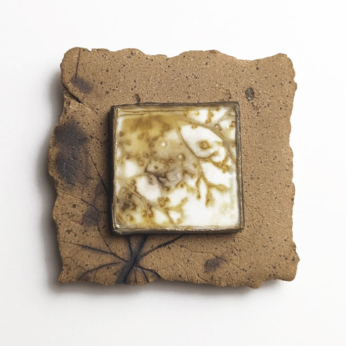 Small ceramic tile with textured blue glaze, with a botanical print encased in wax set in the center. Artwork by Sarah Treanor. 