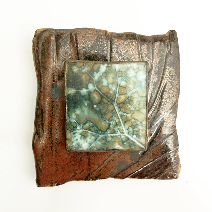 Small, brownish red ceramic tile with an eco print leaf detail encased in wax and mounted in the center. Artwork by Sarah Treanor available at larkandkey.com.