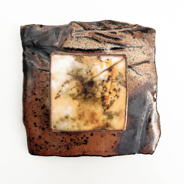 Small, brownish red ceramic tile with an eco print  of a leaf encased in wax and mounted in the center. Artwork by Sarah Treanor available at larkandkey.com.