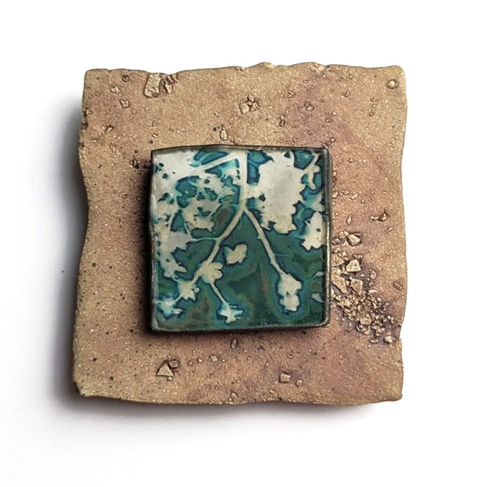 Small ceramic tile with textured blue glaze, with a botanical print encased in wax set in the center. Artwork by Sarah Treanor. 