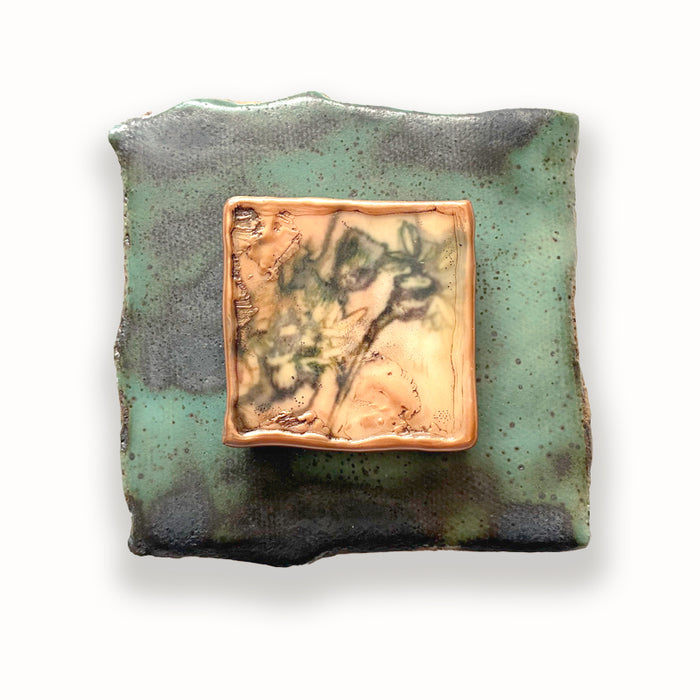 Irregular shaped ceramic tile in green hues, with mixed media floral design in the center. Artwork by Sarah Treanor.