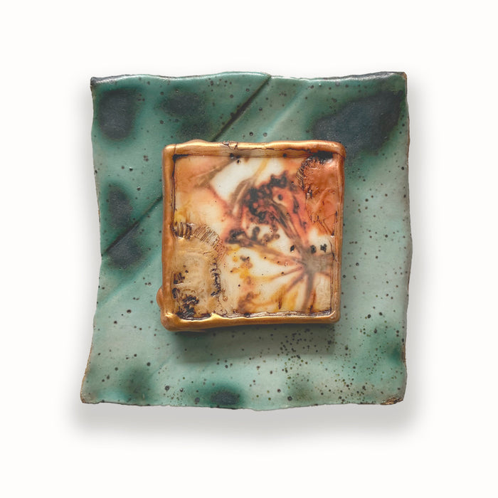 Irregular shaped ceramic tile in green hues, with mixed media golden floral design in the center. Artwork by Sarah Treanor.