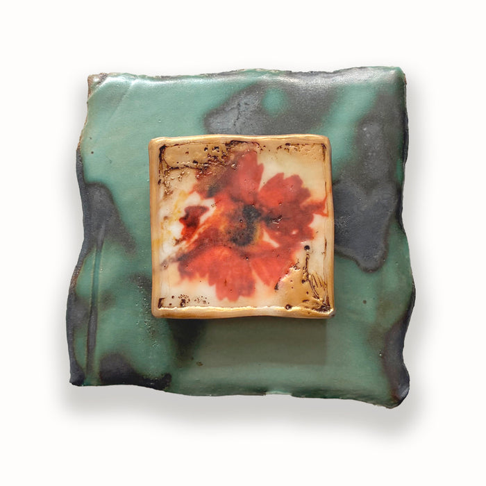 Irregular shaped ceramic tile in green hues, with mixed media orange floral design in the center. Artwork by Sarah Treanor.