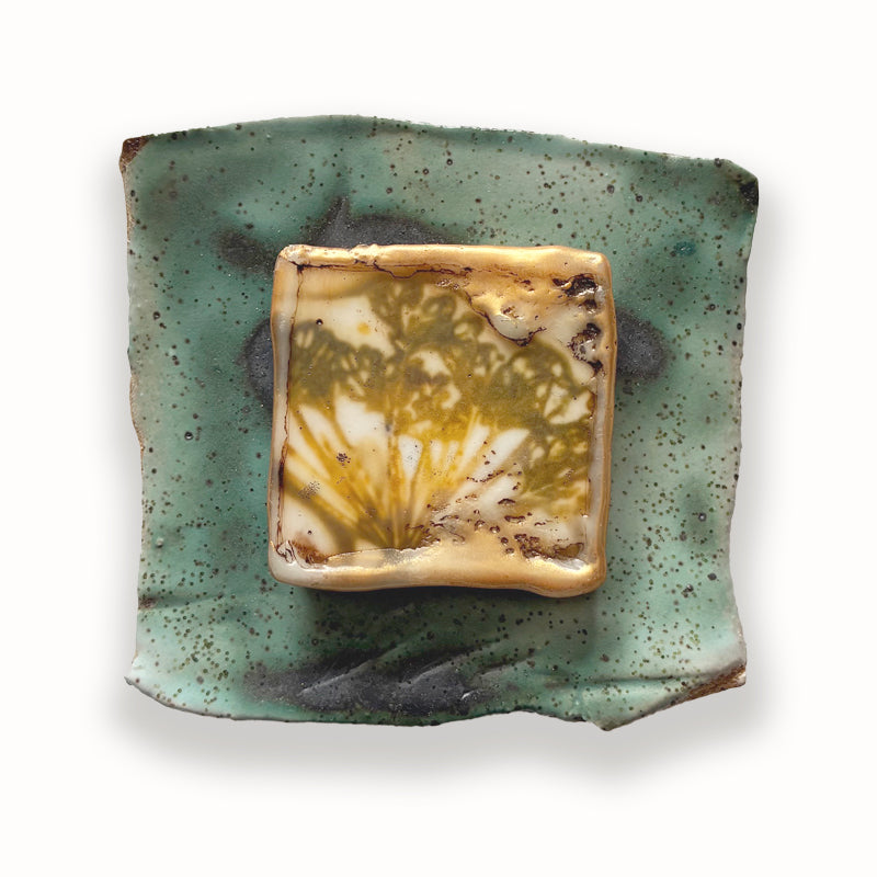 Irregular shaped ceramic tile in green hues, with mixed media golden yellow floral design in the center. Artwork by Sarah Treanor.
