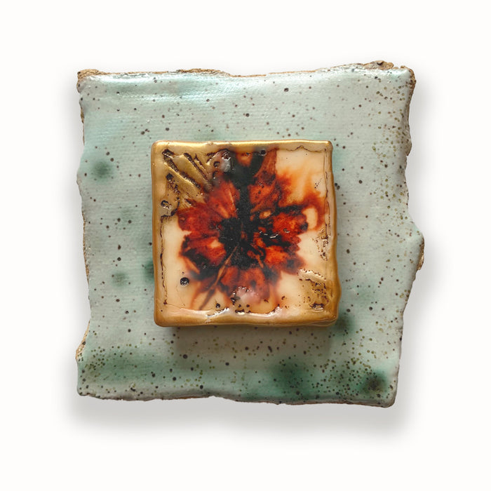 Irregular shaped ceramic tile in light green hues, with mixed media orange floral design in the center. Artwork by Sarah Treanor.