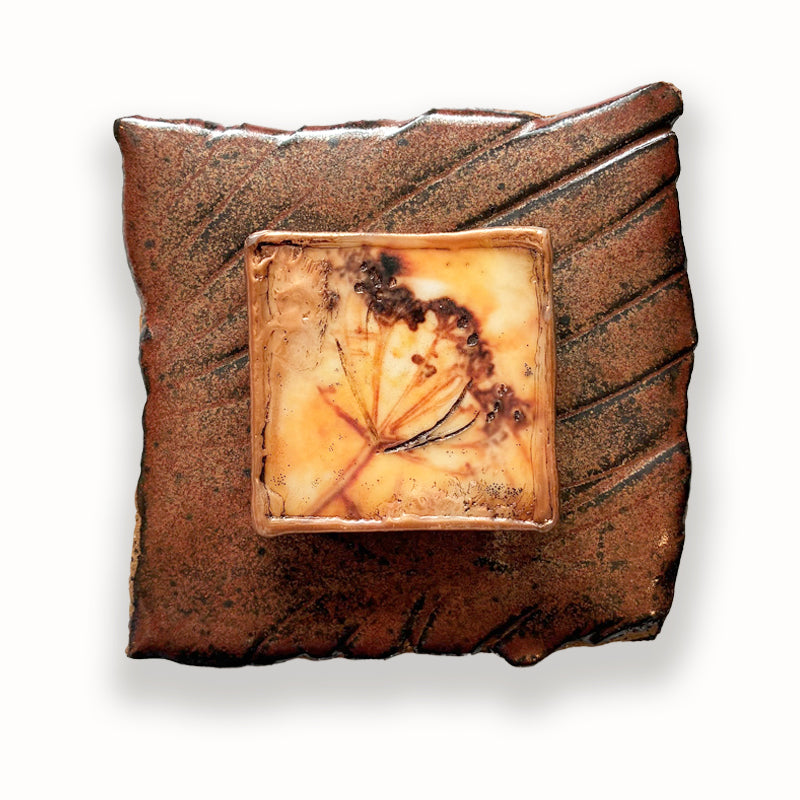 Irregular shaped and textured ceramic tile in brown hues, with mixed media golden floral design in the center. Artwork by Sarah Treanor.