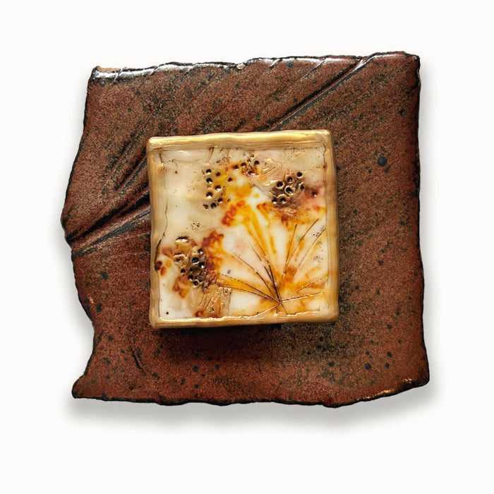Irregular ceramic square with texture and center block featuring mixed golden media floral pattern. Artwork by Sarah Treanor.